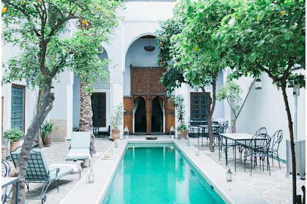 A pool in the middle of a patio with chairs and trees.